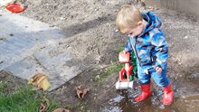 Kind met rode laarzen staat in modder